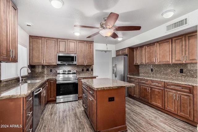 kitchen with appliances with stainless steel finishes, light wood-type flooring, tasteful backsplash, sink, and a center island