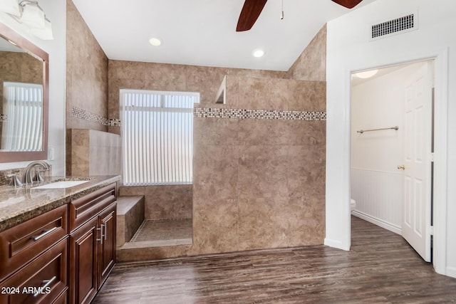 bathroom with vanity, ceiling fan, toilet, tiled shower, and wood-type flooring