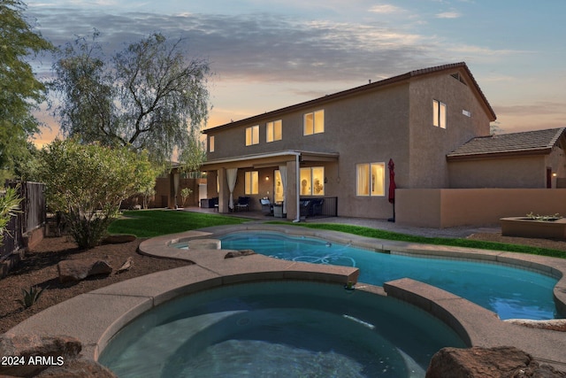 pool at dusk featuring an in ground hot tub and a patio area