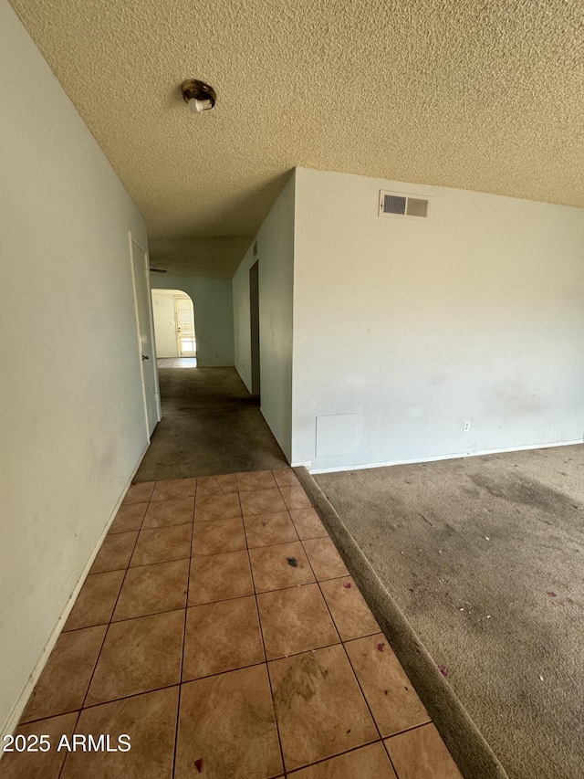 hallway with arched walkways, carpet flooring, a textured ceiling, and visible vents