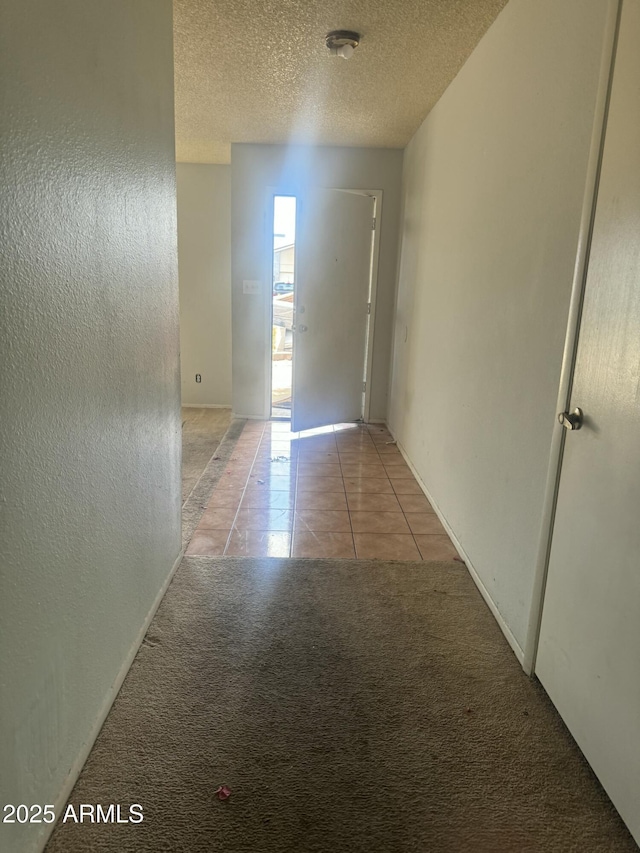 corridor with light tile patterned floors, light carpet, a textured ceiling, and a textured wall