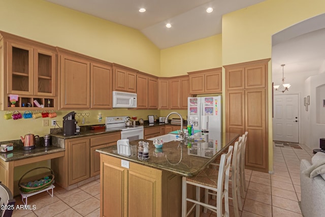 kitchen featuring high vaulted ceiling, light tile patterned flooring, white appliances, brown cabinets, and a center island with sink