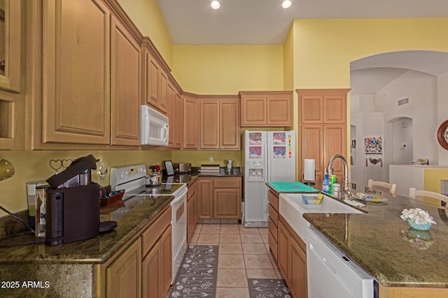 kitchen featuring white appliances, a sink, dark stone countertops, and light tile patterned floors