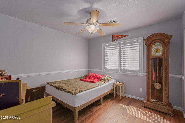 bedroom with ceiling fan, wood finished floors, visible vents, and baseboards