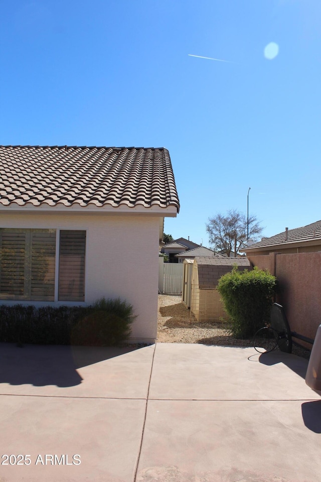 view of property exterior with a patio area, stucco siding, a tiled roof, and fence