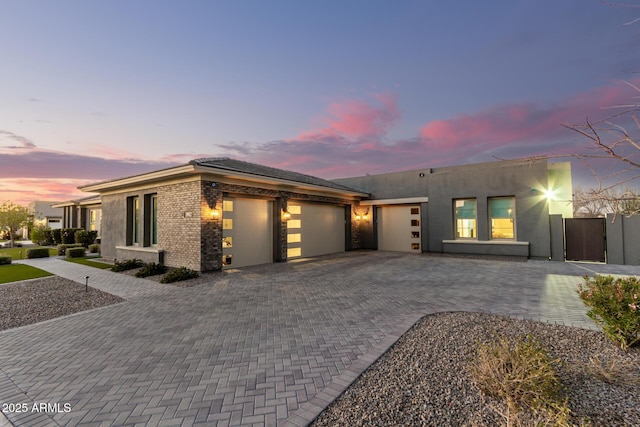 view of front of property featuring decorative driveway, brick siding, an attached garage, and stucco siding