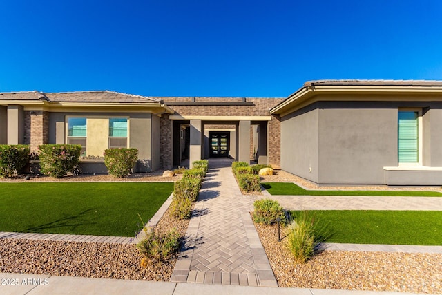 view of front of house featuring solar panels, brick siding, a front yard, and stucco siding