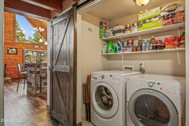 laundry area with wood walls, a barn door, separate washer and dryer, an inviting chandelier, and hardwood / wood-style floors