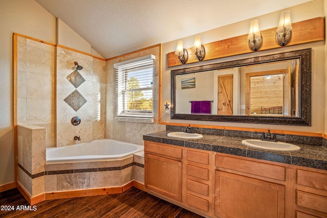 bathroom featuring lofted ceiling, vanity, hardwood / wood-style flooring, a relaxing tiled tub, and a textured ceiling