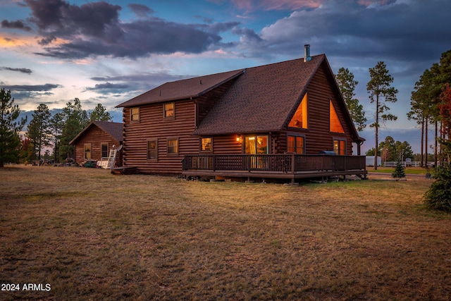 back house at dusk featuring a deck and a lawn