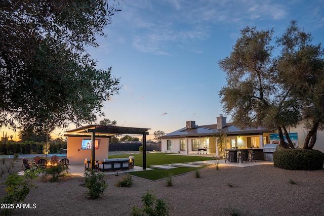 8001 E Voltaire Ave, Scottsdale, AZ 85260 - back of house at dusk with a patio, a lawn, a pergola, a chimney, and solar panels