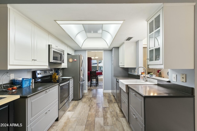 kitchen featuring white cabinets, sink, a notable chandelier, light hardwood / wood-style floors, and stainless steel appliances