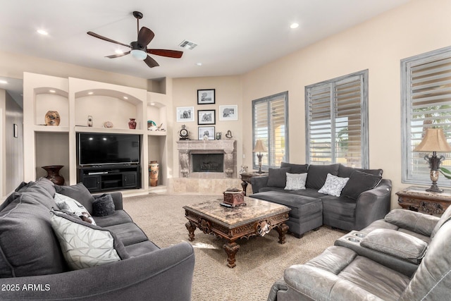 carpeted living room with ceiling fan, built in features, and a fireplace