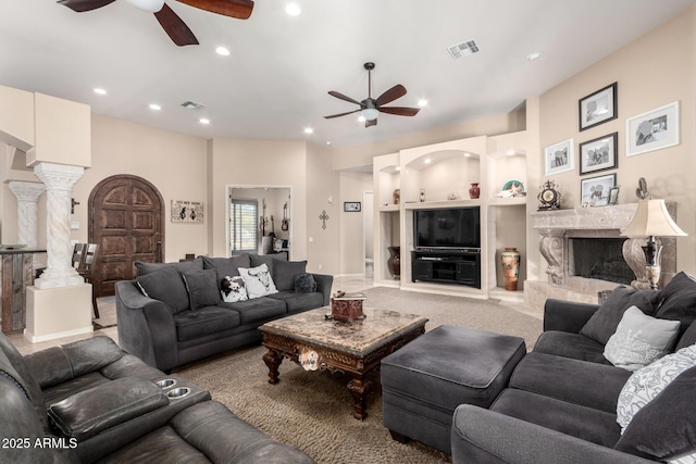 carpeted living room with built in shelves, ceiling fan, a high end fireplace, and decorative columns