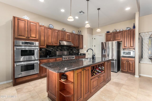 kitchen featuring sink, tasteful backsplash, appliances with stainless steel finishes, pendant lighting, and a kitchen island with sink