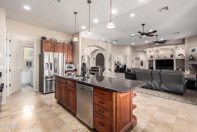 kitchen with sink, a center island with sink, dark stone countertops, appliances with stainless steel finishes, and pendant lighting