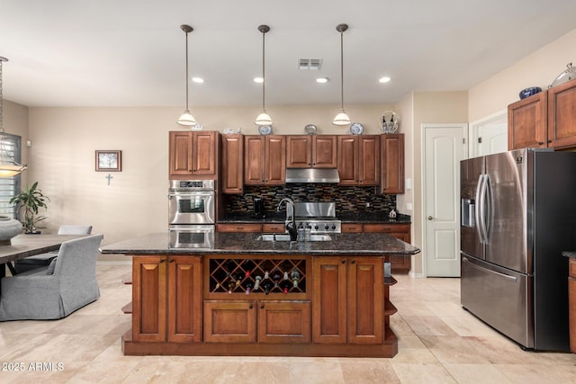 kitchen with stainless steel appliances, hanging light fixtures, a kitchen island with sink, and sink