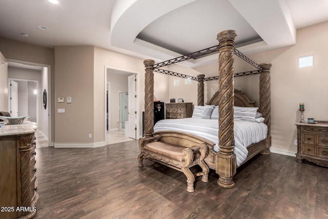 bedroom with dark wood-type flooring, a raised ceiling, and ensuite bathroom