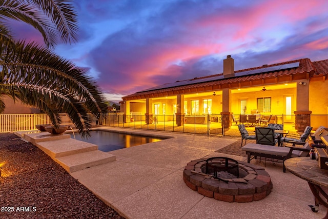 pool at dusk with a patio, ceiling fan, and an outdoor fire pit