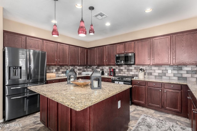 kitchen featuring light stone countertops, decorative light fixtures, decorative backsplash, a center island with sink, and appliances with stainless steel finishes