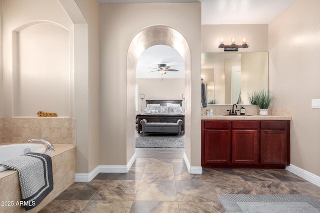 bathroom with a relaxing tiled tub, ceiling fan, and vanity