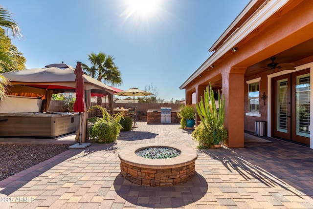 view of patio featuring ceiling fan, exterior kitchen, an outdoor fire pit, a hot tub, and a gazebo