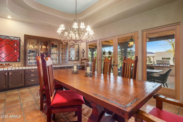 dining space with french doors, a tray ceiling, light tile patterned flooring, and a notable chandelier