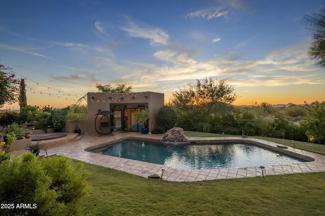 pool at dusk featuring pool water feature, a yard, and a patio area