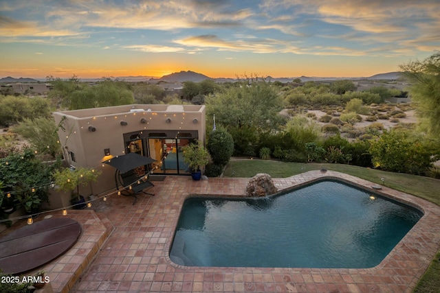 pool at dusk featuring a mountain view, a patio area, and pool water feature