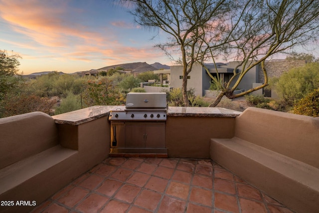 patio terrace at dusk featuring exterior kitchen, a mountain view, and area for grilling