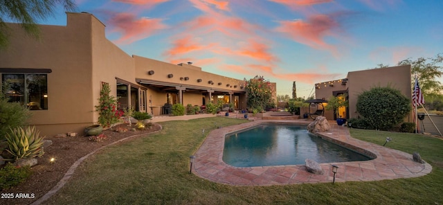 pool at dusk with ceiling fan, a lawn, a patio, and pool water feature