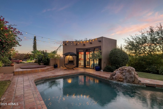 pool at dusk featuring a hot tub and a patio