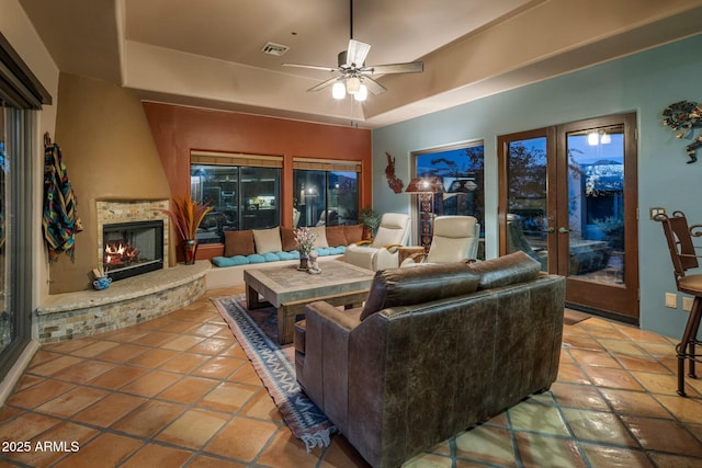 living room featuring ceiling fan, tile patterned floors, a fireplace, and a raised ceiling