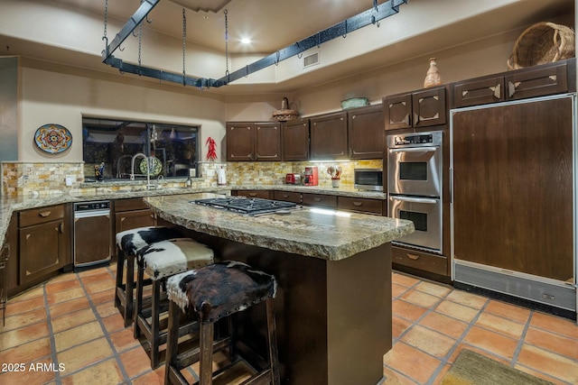 kitchen with a kitchen island, a breakfast bar, backsplash, dark brown cabinetry, and stainless steel appliances