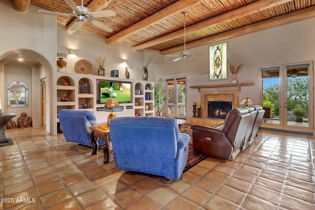 living room with beam ceiling, a tiled fireplace, built in shelves, wooden ceiling, and french doors