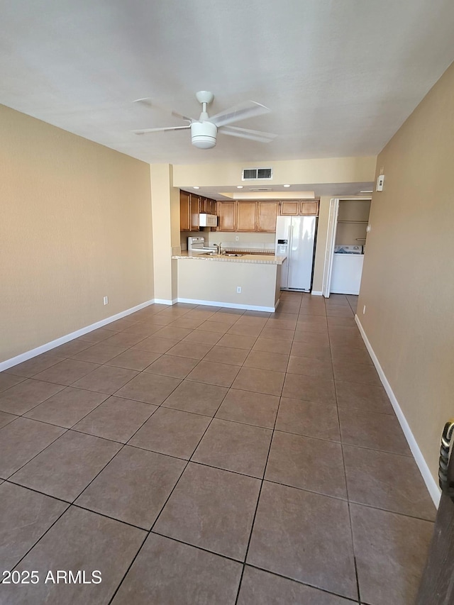 unfurnished living room featuring dark tile patterned floors, sink, ceiling fan, and washer / clothes dryer