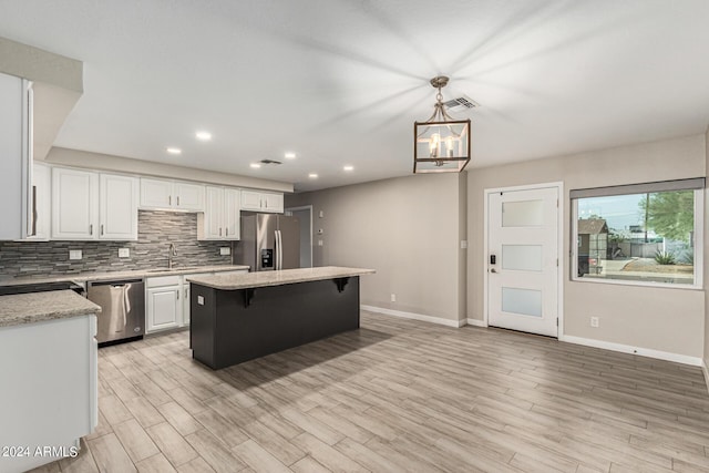 kitchen featuring sink, white cabinetry, stainless steel appliances, a center island, and decorative light fixtures