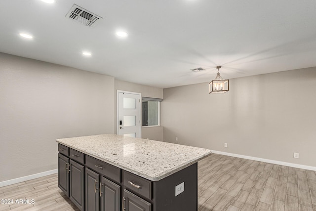 kitchen with light stone countertops, hanging light fixtures, a kitchen island, and light hardwood / wood-style flooring