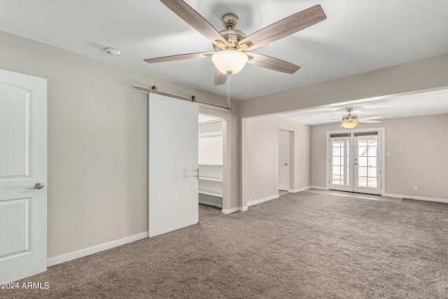 carpeted empty room featuring french doors, ceiling fan, and a barn door