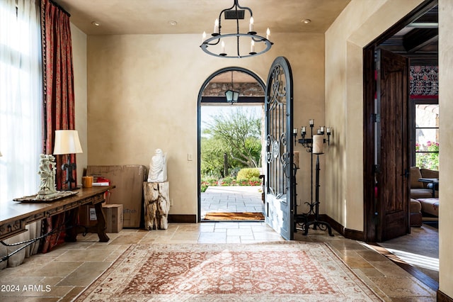 foyer entrance featuring a chandelier, stone tile floors, and baseboards