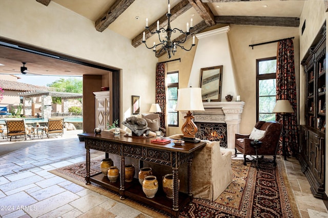 living room featuring beamed ceiling, stone tile flooring, a large fireplace, and ceiling fan with notable chandelier