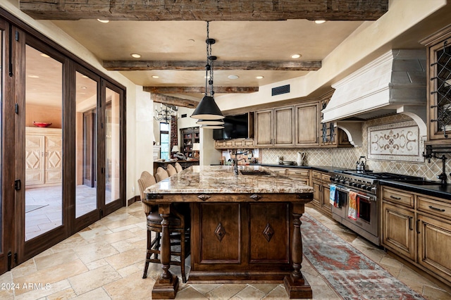 kitchen featuring decorative backsplash, a kitchen island with sink, dark stone counters, decorative light fixtures, and double oven range