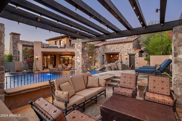 patio terrace at dusk with a pergola, an outdoor living space with a fireplace, and a balcony