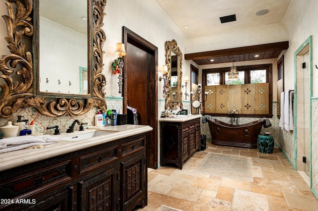 bathroom featuring stone tile floors, two vanities, a sink, and a freestanding bath