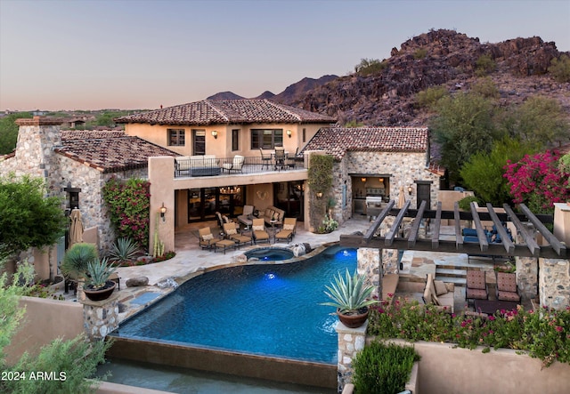 pool at dusk featuring outdoor lounge area, outdoor dining space, a patio area, a mountain view, and a pool with connected hot tub