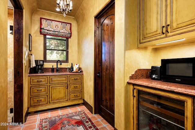 bar with a sink, black microwave, beverage cooler, light tile patterned floors, and a notable chandelier
