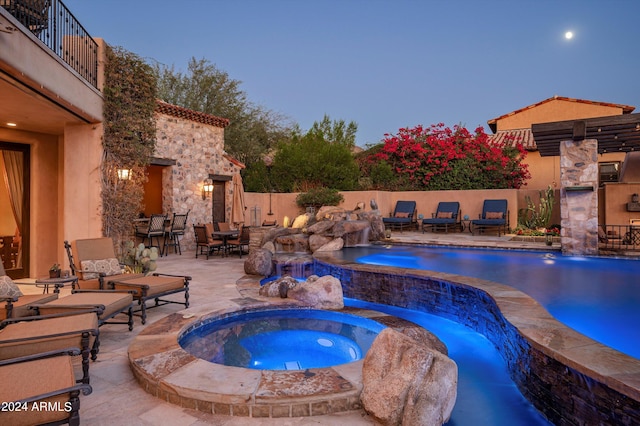 pool at dusk featuring a patio, pool water feature, and an in ground hot tub