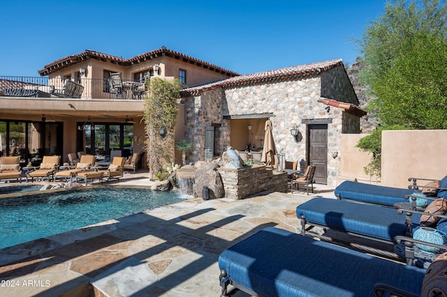 back of property with a pool, a balcony, a patio, and stucco siding