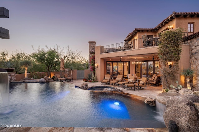 pool at dusk with an in ground hot tub, a patio, pool water feature, and an outdoor living space