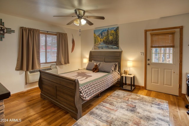 bedroom featuring a wall mounted AC, hardwood / wood-style flooring, and ceiling fan